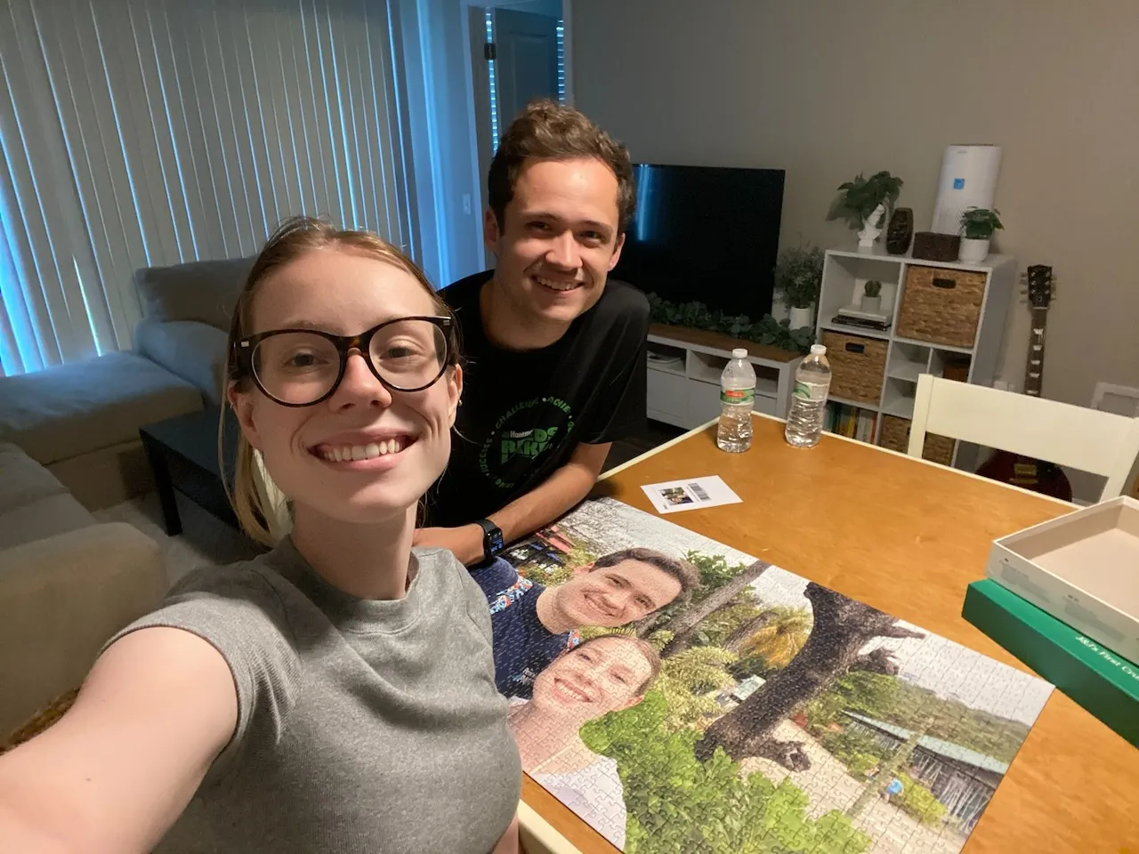 Selfie of Jess and Josh in their first apartment, overlooking a custom puzzle of a photo of them together.