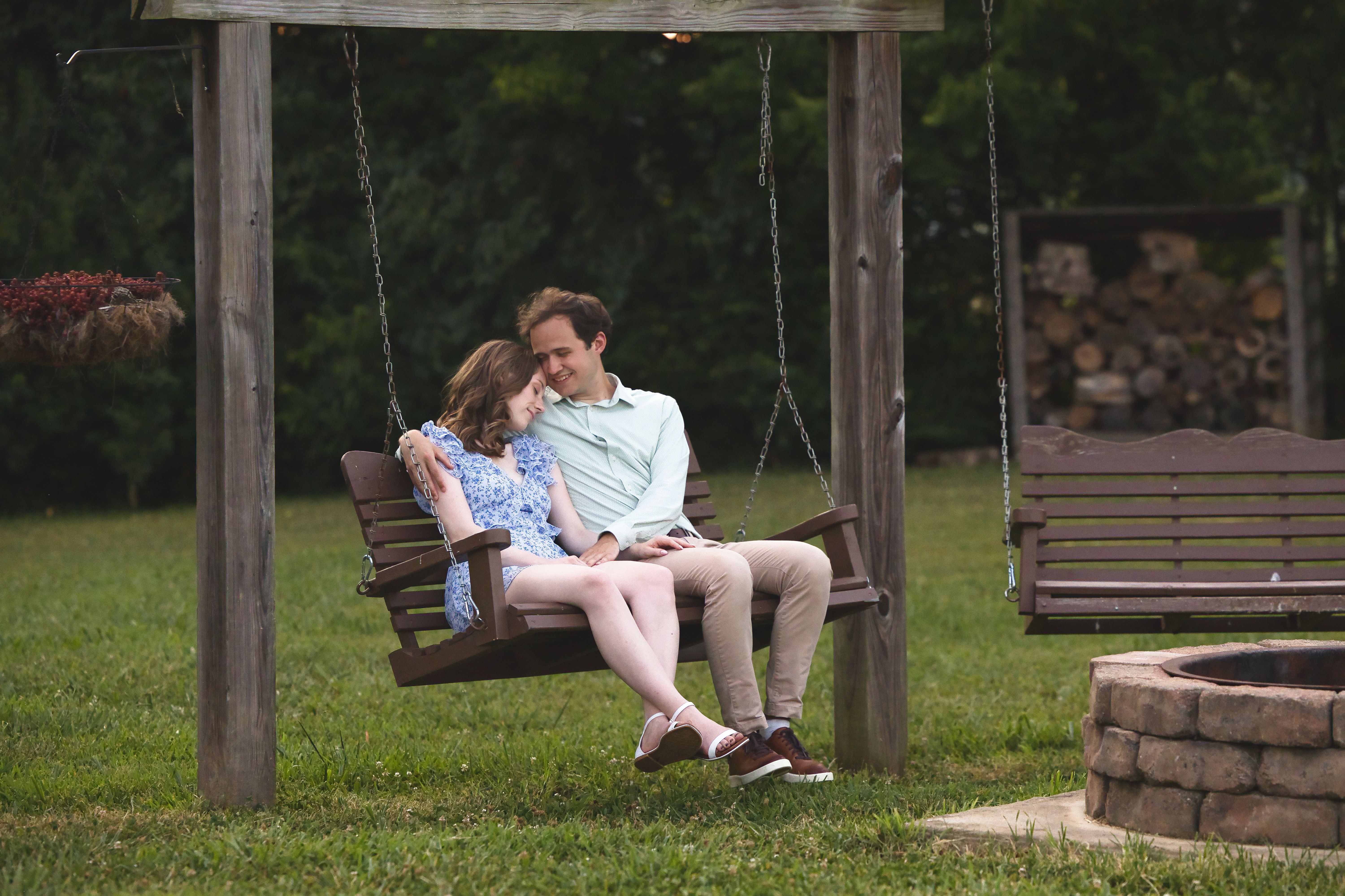 Jess and Josh sitting on a swinging bench. Jess' head is leaning on Josh's shoulder